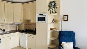 A compact kitchen with cabinets, a microwave, and a chair with a cushion.