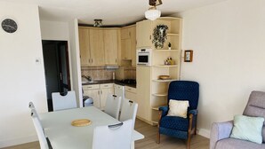 A compact living space with a dining table, chairs, a sofa, a blue armchair, and a kitchenette.