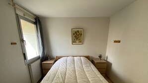 A bedroom with a large bed, two bedside tables, a window with curtains, and a wall-mounted picture.