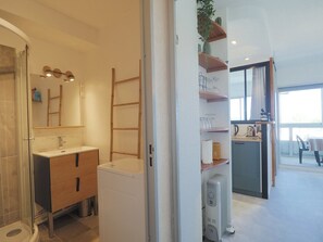 A modern bathroom with a glass shower enclosure, a wooden vanity, and a white washing machine. - Apartment with AC, parking - 5 guests (La Grande-Motte)