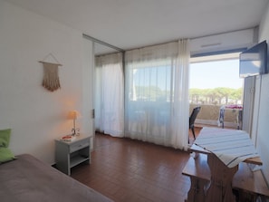 Ein Zimmer mit einem Bett, einem Schreibtisch, einem Sessel, einem Fernseher und einem Balkon mit Blick.