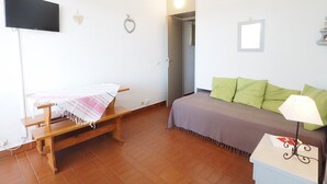 Ein Zimmer mit einem Bett, einer Sitzbank, einem Fernseher und einer Tür zu einem anderen Raum.