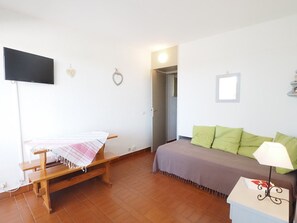 Ein Zimmer mit einem Bett, einer Sitzbank, einem Fernseher und einer Tür zu einem anderen Raum.