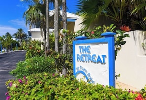 A sign for 'The Retreat at Run Point' with a white background and blue lettering, surrounded by lush greenery and palm trees.