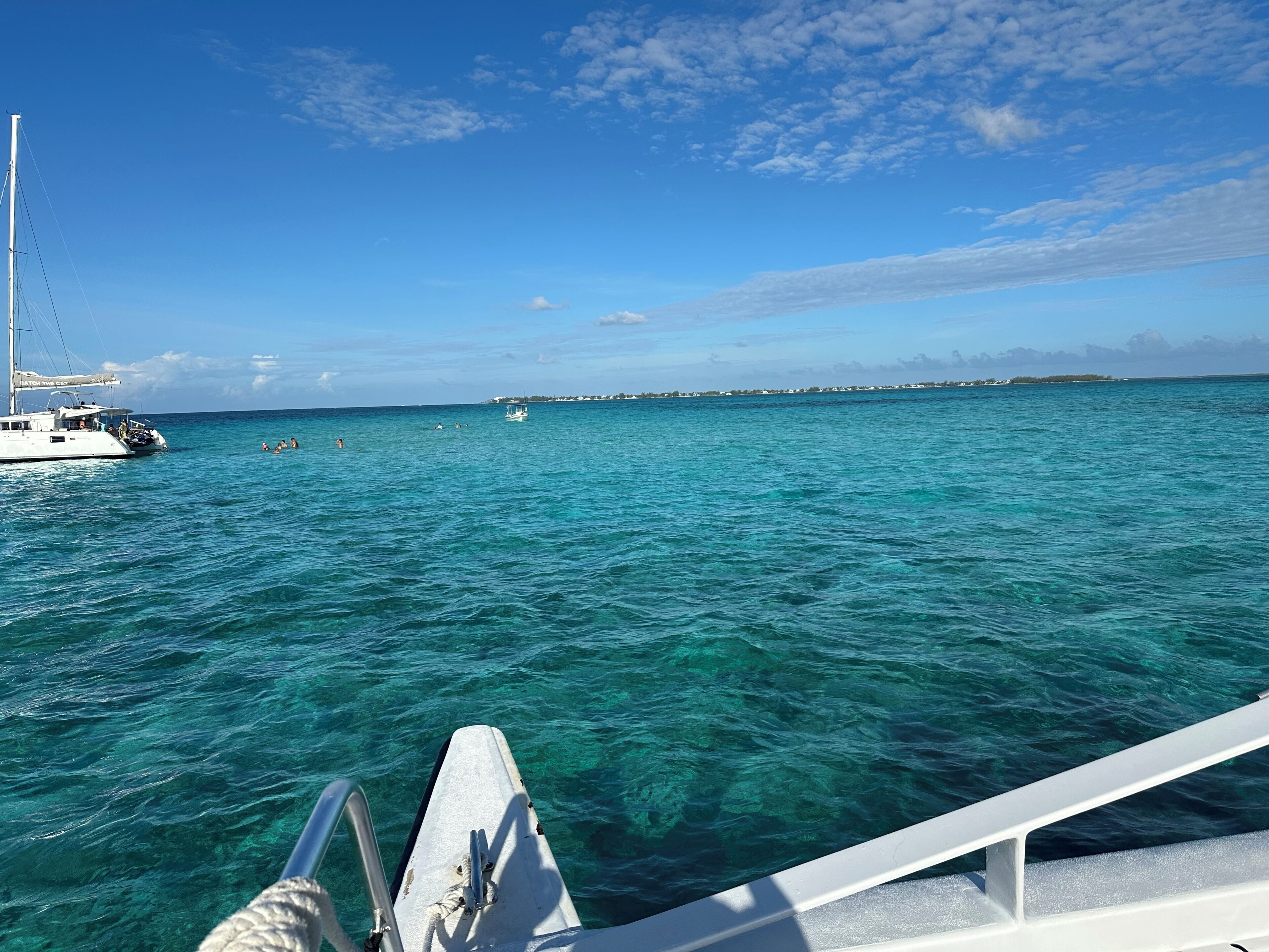 A boat on clear turquoise water with a distant shoreline and a clear sky.