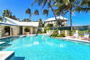 A swimming pool with lounge chairs, palm trees, and a building with a white roof.