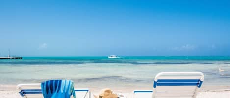 Une plage avec deux chaises longues, une serviette et un chapeau posés sur une petite table.