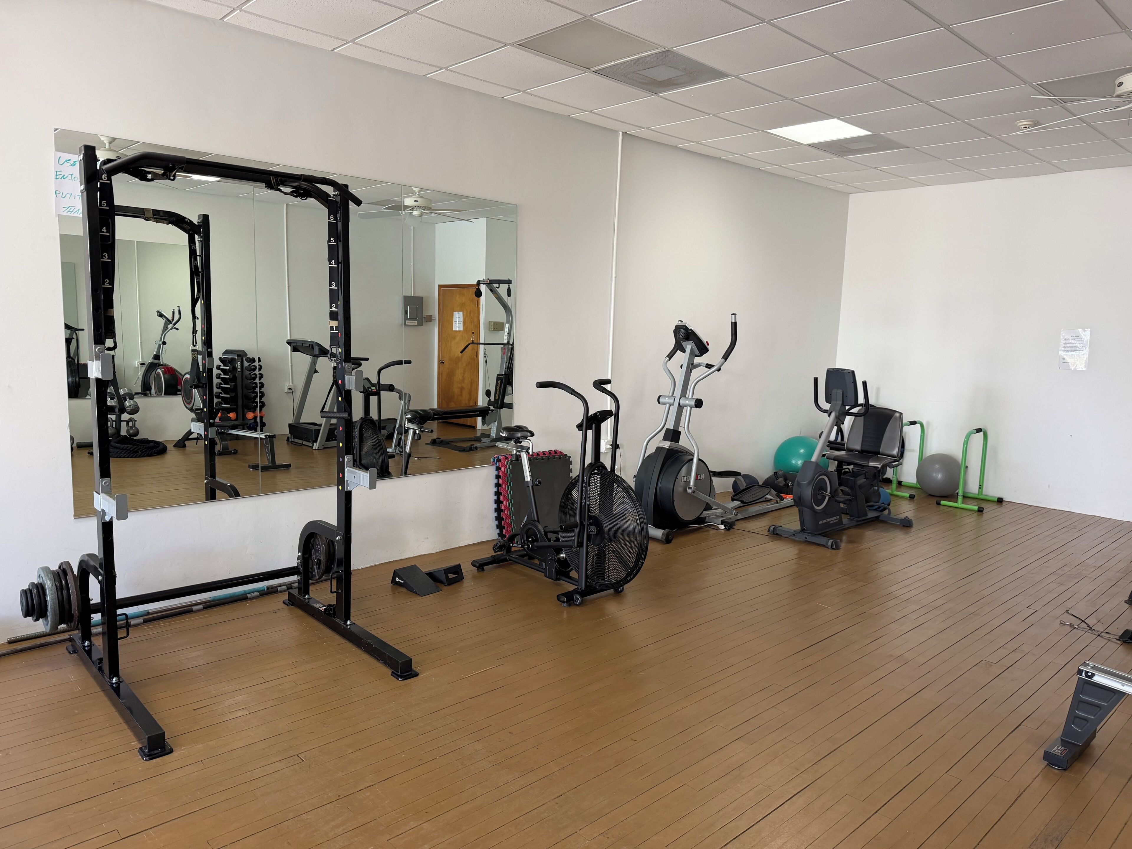 Une salle de sport équipée de matériel d’exercice, dotée d’un grand miroir et d’un plancher en bois.