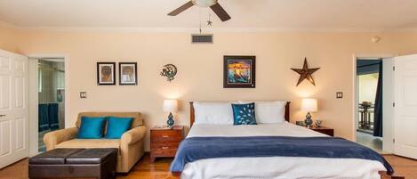 A bedroom with a bed, a sofa, a nightstand, a ceiling fan, and wall decorations.