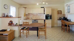 A kitchen with a dining table, chairs, a clock, and a stove.