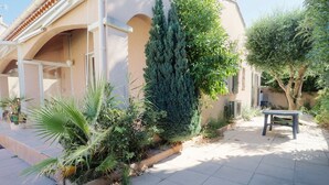 A courtyard with a bench, potted plants, and a building with a tiled roof.