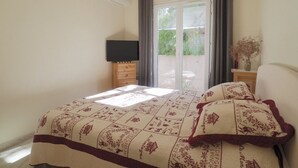 A bedroom with a bed, a TV on a wooden dresser, a sliding glass door to a balcony, and a hanging light fixture.