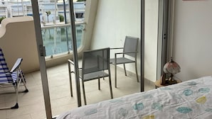 Ein Balkon mit Blick auf Boote, ein Bett mit blattgemusterten Laken und zwei Stühle.