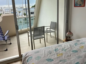 A balcony with a view of boats, a bed with leaf-patterned bedding, and two chairs. - Bright marina, AC, port view - 6 guests (Le Grau-du-Roi)