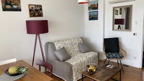 Ein Wohnzimmer mit einer Couch, einem Esstisch mit einer Ananas, einer Stehlampe und Wandbildern.