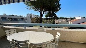 A balcony with a round table and chairs, a view of buildings, and a tree. - Lovely apartment, terrace open view - 4 guests (La Grande-Motte)