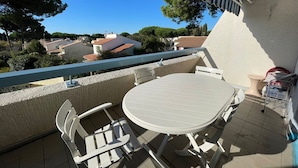 A balcony with a white table and chairs, a striped awning, and a view of houses and trees. - Lovely apartment, terrace open view - 4 guests (La Grande-Motte)