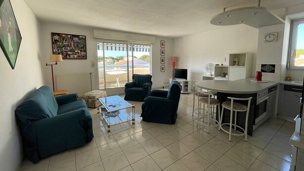 A living room with a sofa, chairs, a coffee table, a TV, and a kitchen area with a fridge, stove, and sink. - Lovely apartment, terrace open view - 4 guests (La Grande-Motte)