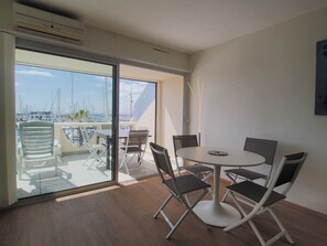 Quarto moderno com mesa redonda e cadeiras, porta de vidro deslizante para uma varanda com vista para barcos e para o mar.