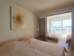 Ein Schlafzimmer mit einem Bett, einem Nachttisch, einer Lampe und einem großen Fenster mit Blick auf einen Jachthafen.