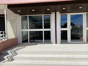 A building entrance with glass doors, a set of stairs, and a wooden overhang. - Charming studio near beach, parking - 2 guests (Le Grau-du-Roi)