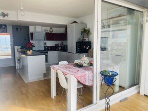 A compact kitchen with a dining area, a small island, and a view through a sliding door. - Apartment with panoramic terrace - 5 guests (La Grande-Motte)
