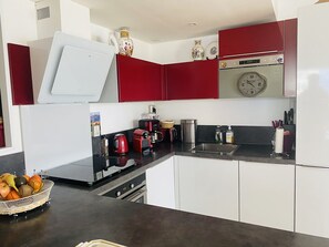 A modern kitchen with white and red cabinets, a stainless steel sink, and a clock on the wall. - Apartment with panoramic terrace - 5 guests (La Grande-Motte)