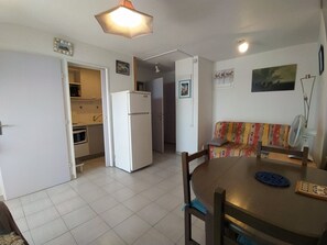 A compact living space with a kitchenette, a dining area, and a sofa. - Apartment with pool, parking, lake view - 4 guests (Le Grau-du-Roi)