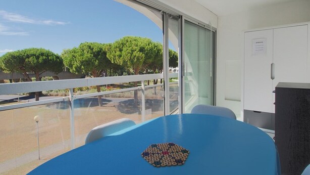 Una habitació amb un finestral gran, una taula blava i vista a arbres.