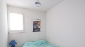 Habitació petita i neta amb un llit, una tauleta de nit, una làmpada, un cartell i una finestra.