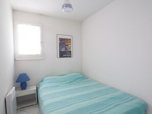 Ein kleiner, sauberer Raum mit einem Bett, einem Nachttisch, einer Lampe, einem Poster und einem Fenster.