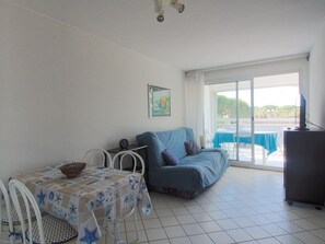 Ein Zimmer mit einem Bett, einem Tisch mit Tischdecke mit Sternenmuster, einem Sessel, einem Fernseher und Blick ins Freie.