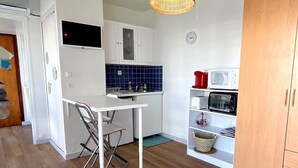 Una cocina compacta con armarios blancos, un microondas, un tostador y una pequeña mesa de comedor con una silla.