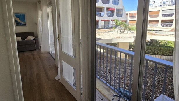Un balcón con barandilla metálica, un sofá y una puerta que da a una habitación.