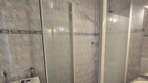 Un baño con ducha de vidrio, lavamanos blanco y piso de baldosas.