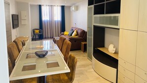 A modern living room with a glass dining table, leather sofas, a TV, and built-in shelving. - Large house with AC in the center - 8 guests (Le Grau-du-Roi)