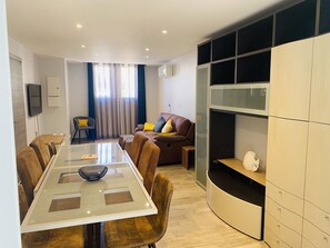 A modern living room with a glass dining table, leather sofas, a TV, and built-in shelving. - Large house with AC in the center - 8 guests (Le Grau-du-Roi)