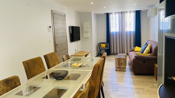 A modern living room with a glass dining table, brown leather sofa, and a TV mounted on the wall. - Large house with AC in the center - 8 guests (Le Grau-du-Roi)
