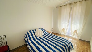A bedroom with a bed, a chair, and a window with curtains. - Large house with AC in the center - 8 guests (Le Grau-du-Roi)