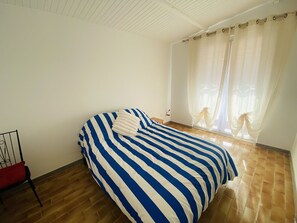 A bedroom with a bed, a chair, and a window with curtains. - Large house with AC in the center - 8 guests (Le Grau-du-Roi)