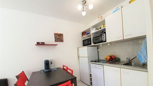 Eine kompakte Küche mit Esstisch, Stühlen, Mikrowelle, Kühlschrank und Spüle.