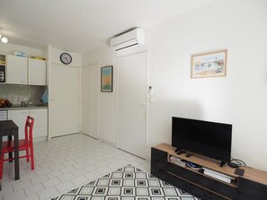 A compact living space with a kitchenette, a dining area, a TV, and a patterned rug. - Apartment with AC, parking, pool - 6 guests (La Grande-Motte)