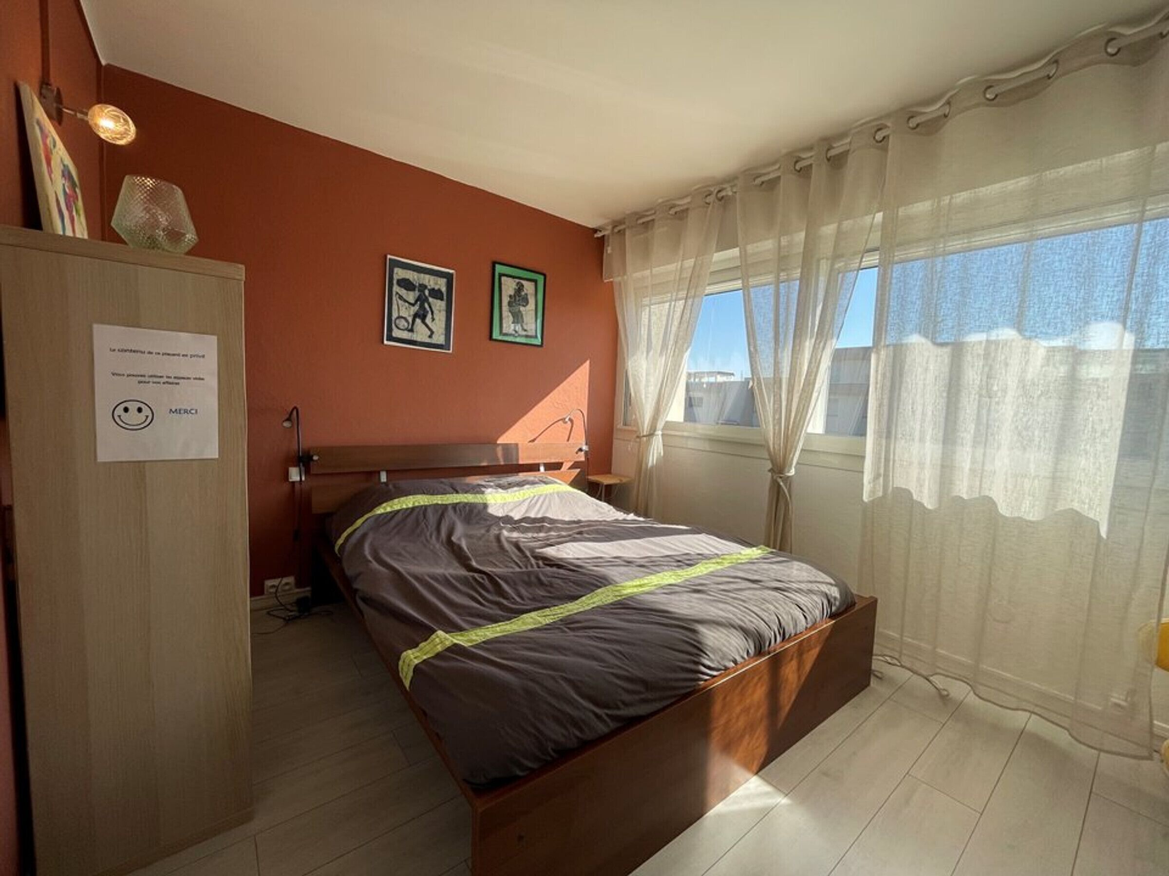 A bedroom with a bed, a nightstand, a wardrobe, and a window with curtains.