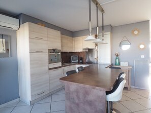 Eine moderne Küche mit einer zentralen Kochinsel, Edelstahlgeräten, Pendelleuchten und einem großen Spiegel an der Wand.