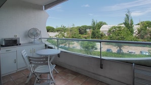Un balcone con tavolo e sedie, una ventola e vista su un parcheggio e zone verdi.