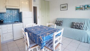 Una cucina compatta con mobili bianchi, uno schienale azzurro rivestito di piastrelle, un tavolo da pranzo con tovaglia blu e un divano celeste con cuscini decorati.