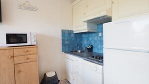 Una cucina compatta con forno a microonde, fornello, lavello e pensili bianchi.