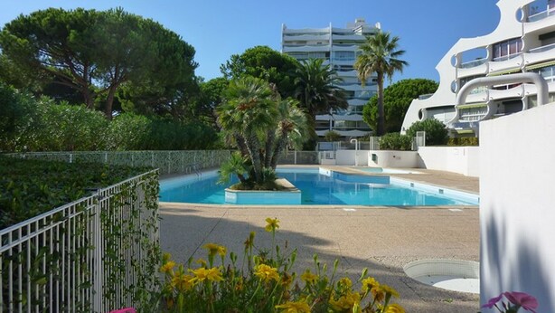 Una piscina circondata da un giardino, un edificio bianco con balconi e un edificio alto sullo sfondo.
