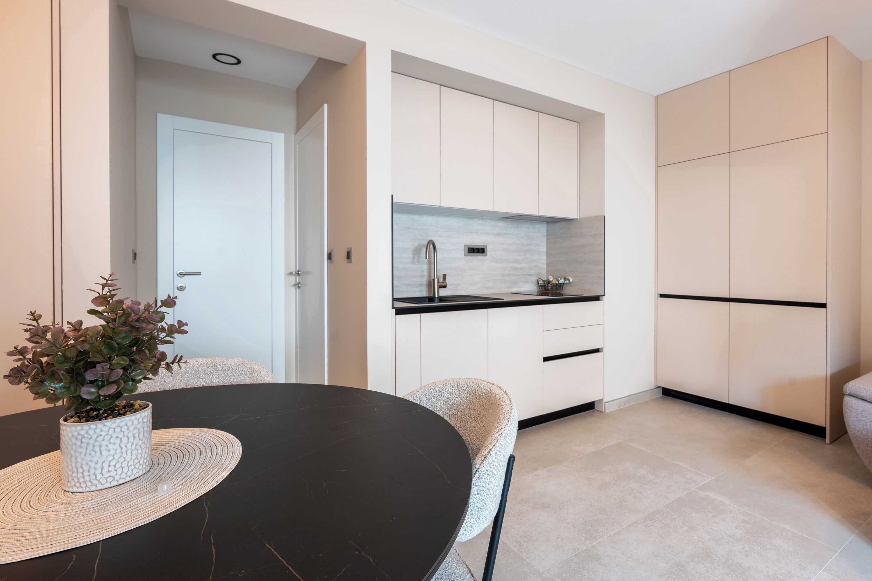 Une cuisine moderne avec des meubles blancs, un plan de travail noir et un petit îlot central agrémenté d’une plante.
