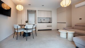 A modern kitchen with white cabinets, a dining area with a table and chairs, and a seating area with a sofa and ottomans. - Villa Merkur -apartment 1 (Makarska)